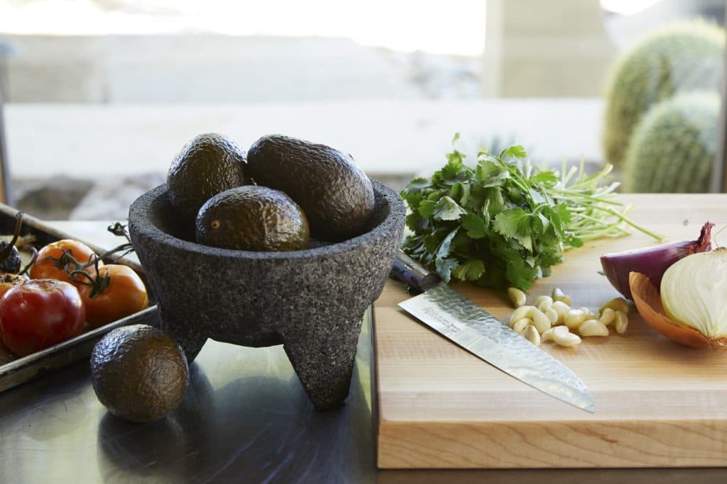 avocados cilantro tomatoes garlic and onion on a table to cut